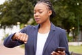 Black woman, phone and time management for business schedule while outdoor with a watch at a park waiting for a meeting Royalty Free Stock Photo