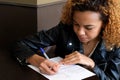 A young pretty dark-haired girl in a black leather jacket puts a signature on the document. The black woman signs a Royalty Free Stock Photo