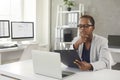 Black woman sitting at her desk in office, reading business documents and thinking Royalty Free Stock Photo