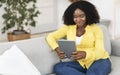 Black woman sitting on sofa, using tablet Royalty Free Stock Photo
