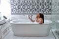 Black woman taking bath with bubbles in bathroom interior, singing in shower handle, have fun Royalty Free Stock Photo