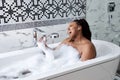 Black woman taking bath with bubbles in bathroom interior, singing in shower handle, have fun Royalty Free Stock Photo