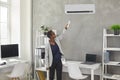 Black woman uses a remote control to switch a modern air conditioner in the office Royalty Free Stock Photo