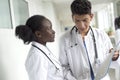 Black woman and white male doctors. A pair of young doctors of mixed race in white coats with a folder in their hands discussing