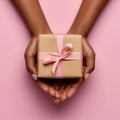 Black womans hands holding a present gift box with bow against a light pink background. Overhead view. Close up. Mothers, Women Royalty Free Stock Photo