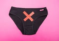 Black women`s panties with a red cross on a pink background. Concept of female gynecological diseases, cervical erosion and