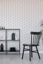 Black wooden chairs next to metal shelf with vases, plate and accessories on empty wall wall with unique wallpaper, real photo Royalty Free Stock Photo