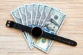 Black wrist electronic watch with stacks of dollar bills on a wooden background close-up