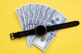 Black wrist electronic watch with stacks of dollar bills on a yellow background close-up