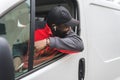 Black young adult delivery man sitting in driver seat of white van leaning out the window smiling looking away from Royalty Free Stock Photo