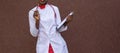 Black young woman doctor, in a white coat, with a phonendoscope, holds a folder for medical papers in a rue, against the Royalty Free Stock Photo