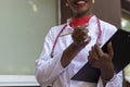 Black young woman doctor, in a white coat, with a phonendoscope, holds a folder for medical papers in a rue, against the Royalty Free Stock Photo