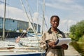 Black young woman holding clipboard and smiling at camera working in yacht docks