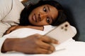 Black young woman using cellphone while lying in bed at home Royalty Free Stock Photo