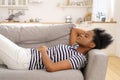 Black young woman wear stripped t-shirt resting sleeping on couch at home closed eyes taking a break Royalty Free Stock Photo