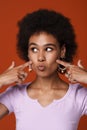 Black young woman wearing rings pointing fingers at her cheeks