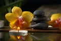Black zen stones, candles and yellow orchids on a wooden plank on the surface of the water. SPA, relaxation, meditation