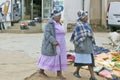 Black Zulu women in brightly colored clothing walk past street vendors in Zulu village, Zululand, South Africa