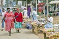 Black Zulu women in brightly colored red dresses walk past produce vendors in Zulu village in Zululand, South Africa Royalty Free Stock Photo