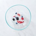 Glass bowl with different fresh berries and ice cubes on a gray marble background with space for text. Top view Royalty Free Stock Photo