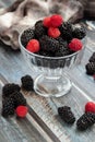 Blackberries and raspberries in a glass container on a wooden background. Textile. Wild flowers, daisies. Vertical position of the Royalty Free Stock Photo