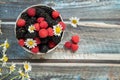 Blackberries and raspberries in a white container on a wooden background. Textile. Wild flowers, daisies. Horizontal position of Royalty Free Stock Photo