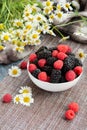 Blackberries and raspberries in a white container on a wooden background. Textile. Wild flowers, daisies. Vertical position of the Royalty Free Stock Photo