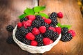 Blackberry and raspberry in a white basket under sunlight on a wooden background