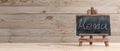 Blackboard on folding wooden easel and menu inscription, against wooden background with copy space and text, banner, 3d