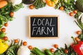 Blackboard with handwritten text `Local Farm` and assorted vegetables and herbs on white background