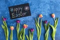 Blackboard with Happy Easter greeting. Tulips on dark blue background. Holiday decorations, Easter concept background