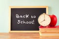 Blackboard with the phrase back to school, apple clock and stack of books. filtered image
