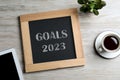 Blackboard with phrase GOALS 2023 on wooden background, flat lay