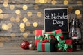 Blackboard with phrase St. Nicholas Day, gift boxes and festive decor on wooden table, space for text. Bokeh effect Royalty Free Stock Photo