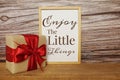 Blackboard with the text ENJOY THE LITTLE THINGS with gift box and red ribbon on wooden background Royalty Free Stock Photo
