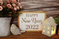 Blackboard With The Text HAPPY NEW YEAR 2022 Decorate With LED Candle In House Lantern And Bird Statue On Wooden Background