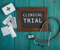 Blackboard with text & x22;Clinical trial& x22;, pills and stethoscope on blue wooden background