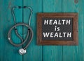 Blackboard with text & x22;Health is wealth& x22; and stethoscope on blue wooden background