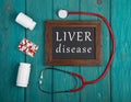 Blackboard with text & x22;Liver disease& x22;, pills and stethoscope on wooden background