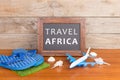 blackboard with text & x22;Travel Africa& x22;, plane, flops, seashells