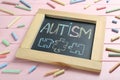 Blackboard with word Autism and drawn jigsaw puzzle pieces surrounded by colorful chalks on pink wooden background