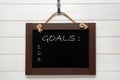 Blackboard with word GOALS and empty checklist on hanging on white wooden background