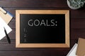 Blackboard with word GOALS and empty checklist on wooden background, flat lay