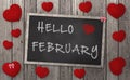 Blackboard With Words Hello February, Surrounded By Red Hearts On Weathered Wooden Background
