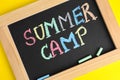 Blackboard with words SUMMER CAMP and colorful chalk on yellow background