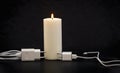 Blackout concept. Electric charger with cable near lighting candle on dark background Royalty Free Stock Photo