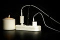 Blackout concept. Electric charger with cable near lighting candle on dark background Royalty Free Stock Photo