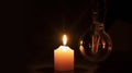 Blackout concept, turned off light bulb with no electricity hanging next to a burning candle Royalty Free Stock Photo