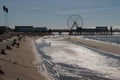 People sitting on sea wall with sandy beach and pier in the background Royalty Free Stock Photo