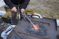 Blacksmith hand holds forceps with a metal billet in a burning forge glowing it red. At the smithy workshop